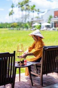 会安Chez Mimosa Rice Farm Hoi An - New address DX18, Thanh Nhut, Cam Thanh的坐在长凳上戴帽子的女人