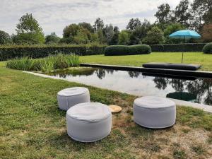 TessenderloB&B De Levensboom的三个白凳坐在池塘附近的草地上
