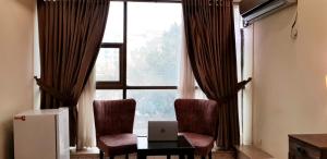 伊斯兰堡Islamabad Premium Hotel的客房设有带2把椅子的窗户和1台笔记本电脑的桌子。