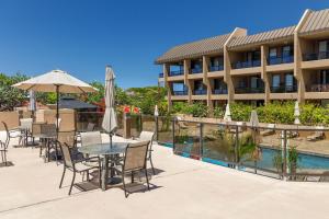 科纳Kona Pacific B409的酒店庭院设有桌子和遮阳伞,毗邻游泳池