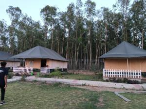 萨哈兰普尔Pulastya Wellness Resort的森林前方的两座茅屋,屋顶黑色