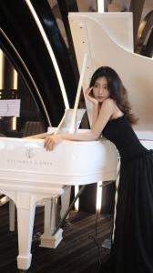 头顿Premier Pearl Hotel Vung Tau的坐在白钢琴上的身着黑色裙子的女人