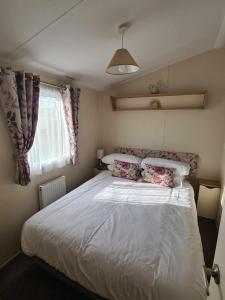 法利Happy Days Caravan Primrose Valley的卧室配有带枕头的白色床和窗户。