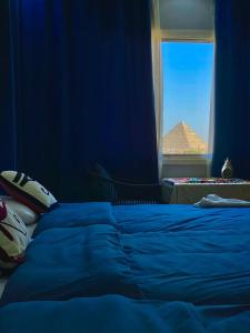 开罗Three pyramids view INN的蓝色的卧室设有一张床和一个带金字塔的窗户