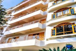 西姆拉Goroomgo Kalra Regency - Best Hotel Near Mall Road with Parking Facilities - Luxury Room Mountain View的白色的建筑,拥有黄色的窗户和树木