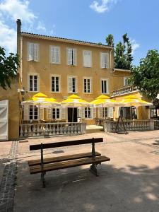 La RoquebrussanneHôtel de la Loube的黄色雨伞建筑前的长凳