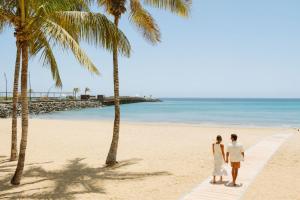 阿雷西费阿瑞斯弗格兰酒店及水疗中心的一对夫妇站在棕榈树海滩上