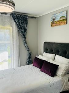 内尔斯普雷特Lakhe Lethu Apartment: Green Valley Estate的一间卧室配有一张带紫色枕头的床和窗户。
