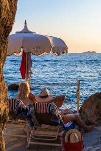 普莱伊亚诺特里托尼大酒店的两人坐在海滩上一把遮阳伞下的椅子上