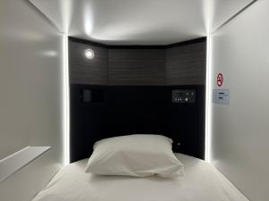 东京カプセルホテル鈴森屋 Capsule Hotel Suzumoriya的一间卧室配有一张白色的床和黑色床头板