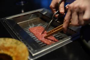 京都Nazuna Kyoto Tsubaki St.的烤架上用剪刀烧肉的人