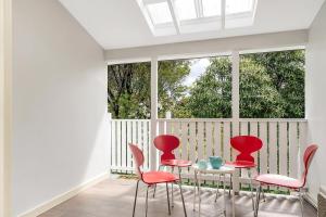 肯图巴Charming Blue Mountains Cottage - Katoomba的阳台配有红色椅子、桌子和窗户。