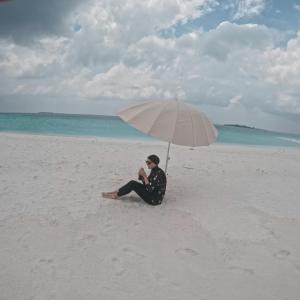 MahibadhooRaalhu Fonu Maldives的坐在海滩上,在伞下