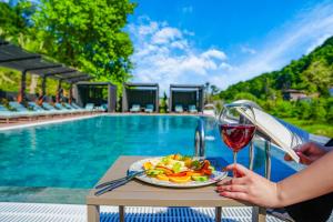埃利特温泉Vital Thermal Hotel & SPA的持着一杯葡萄酒和一盘食物的女人在游泳池旁边