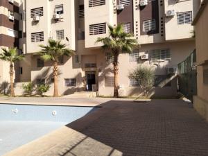 马拉喀什Les portes de Gueliz - apartment 6 people的一座棕榈树环绕的建筑,位于游泳池前