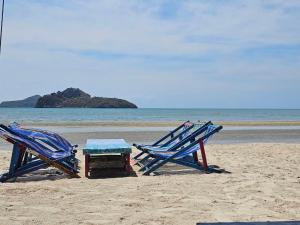 华欣Ocean Blue Huahin Guesthouse的海滩上的两把椅子和一张桌子