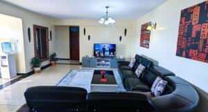 内罗毕Tribal Themed 3BR Penthouse的客厅配有黑色真皮沙发和电视