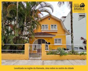 布卢梅瑙Casa Amarela Blumenau Hospedagem Alternativa的黄色房子,有栅栏和棕榈树
