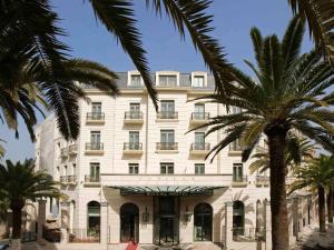 奥兰Royal Hotel Oran - MGallery Hotel Collection的一座白色的大建筑,前面有棕榈树