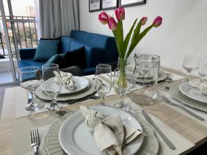 圣保罗Apartamento novo decorado com sacada e linda vista da Cidade的餐桌,配有盘子、玻璃杯和粉红色郁金香