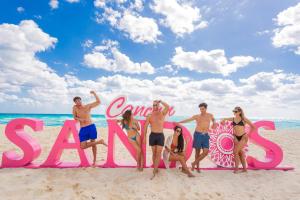 坎昆Sandos Cancun All Inclusive的一群人站在海滩上的一个标志前