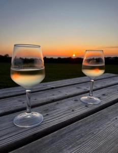 Les Moitiers-dʼAllonneCamping Les Ronds Duval face aux îles anglo-normandes的木桌边的两杯葡萄酒,享有日落美景