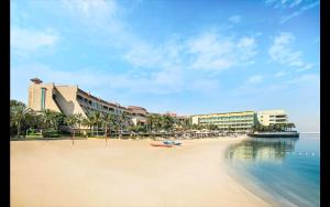 阿布扎比Al Raha Beach Hotel - Gulf View Room DBL - UAE的一片拥有部分建筑的海滩,水面和冰 ⁇ 