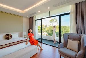 下龙湾View View Villas Hạ Long 6A01 - 8Br -Pool的坐在酒店房间床上的红色衣服女人