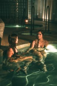麦德林Wellcomm Spa & Hotel的两个女人晚上坐在游泳池里