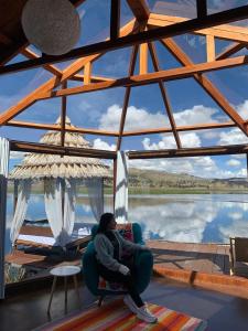 普诺Titicaca Magical Lodge Peru的坐在椅子上的女士,坐在带大窗户的房间里
