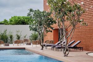 富国Villa Wyndham Phu Quoc的砖墙旁的游泳池,设有椅子和树木