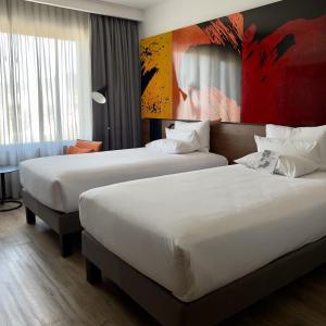 圣地亚哥Novotel Santiago Providencia的酒店客房设有两张床,墙上挂有绘画作品