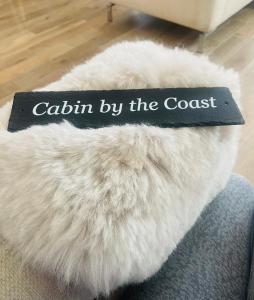 爱丁堡Cabin by the coast的一本书,放在白色皮垫上,上面有海岸边的文字小屋