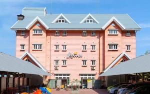 涩川市Ikaho Kids Paradise Hotel - Vacation STAY 56072v的一座大型粉红色建筑,前面有汽车停放