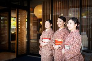 松山Dogo Onsen Yachiyo 道後温泉八千代的三名身着和服的女人站在一座建筑物外面