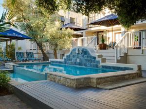 斯泰伦博斯Protea Hotel by Marriott Dorpshuis & Spa Stellenbosch的一个带楼梯、蓝色椅子和遮阳伞的游泳池