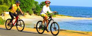 瓦伊卡尔Even Beach Resort的两个人骑着自行车沿着靠近大海的公路行驶