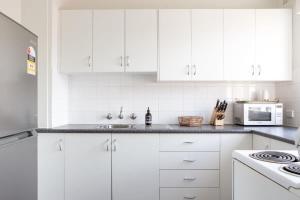 悉尼Sunny Apartment in Quiet and Green Neighbourhood的白色的厨房配有白色的橱柜和微波炉
