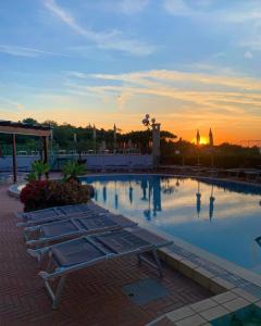 伊斯基亚Resort Villa Flavio的日落前带两个长椅的游泳池