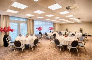 汉堡汉堡市北莱昂纳多酒店的宴会厅配有白色的桌椅和红色的鲜花
