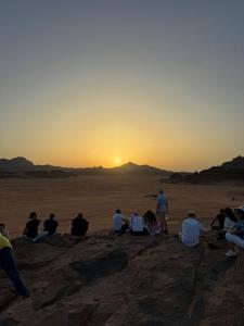 瓦迪拉姆Shakria Bedouin Life Camp的一群坐在沙漠里观看日落的人