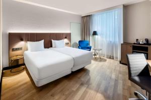 卢森堡卢森堡NH酒店的酒店客房设有一张白色大床和一张蓝色椅子。