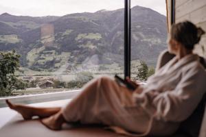菲根贝格ASTER Boutique Hotel & Chalets的坐在窗台上,望着山的女人