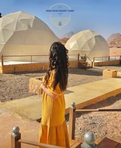 瓦迪拉姆Wadi Rum desert camp的穿着黄色衣服的年轻女孩,看着圆顶