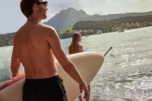 卢塞恩HERMITAGE Lake Lucerne - Beach Club & Lifestyle Hotel的水里拿着冲浪板的男人和女人
