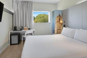 Les Franqueses del VallèsB&B HOTEL Barcelona Granollers的卧室配有白色的床、书桌和窗户。