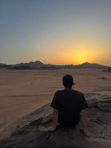 瓦迪拉姆Dream Bedouin life camp的坐在沙漠中观看日落的人