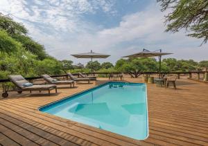 MababeHideaways Mogotlho Safari Lodge, Khwai River的木制甲板上配有椅子和遮阳伞的游泳池