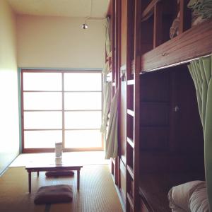宫津市天桥立青年旅舍的窗户前设有一张床和一张桌子的房间