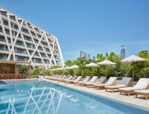 阿布扎比The Abu Dhabi EDITION的一座带躺椅和遮阳伞的游泳池位于大楼旁